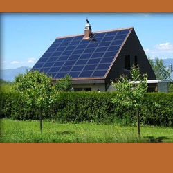 A grey house with a roof covered in solar panels, blue sky, a hedge, trees and grass with an orange background.