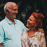 An image of a retired male and female couple standing together, looking at eachother and smiling.