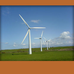 4 white windmills in a line in a field of grass, blue sky behind the windmills and an orange background.